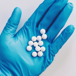 some_white_round_pills_on_a_hand_with_blue_rubber_glove